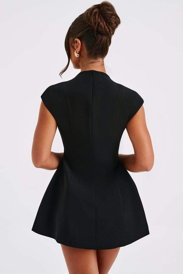 A woman models a black structured mini blazer dress featuring a high mock neck, a deep plunging keyhole cutout, extended cap sleeves, and a flared A-line skirt with flap pockets.