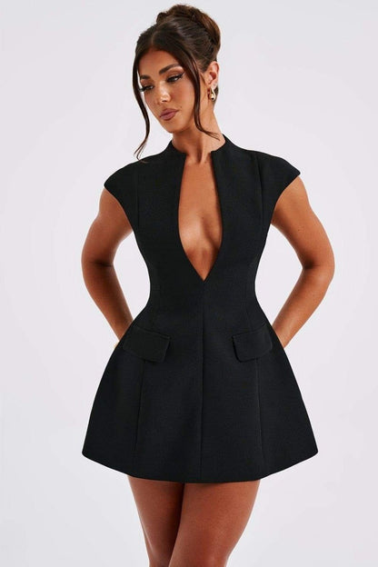 Woman in a black structured tuxedo mini dress with a deep plunging neckline, cap sleeves, and a flared skirt, posing against a white background.
