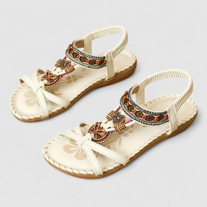 White Athena - Flat open-toe sandals featuring intricate beaded medallions, contrast stitching along the sole, and an elasticized slingback strap.