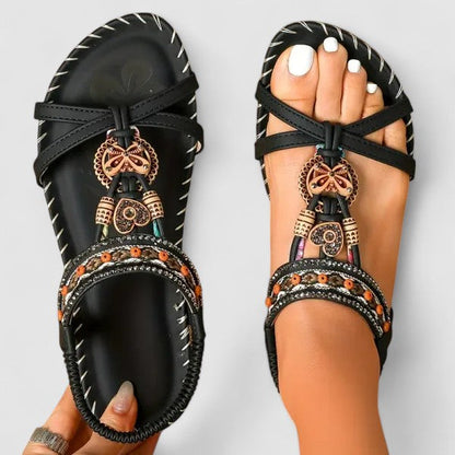 Graphite Black - Flat open-toe sandals featuring intricate beaded medallions, contrast stitching along the sole, and an elasticized slingback strap.