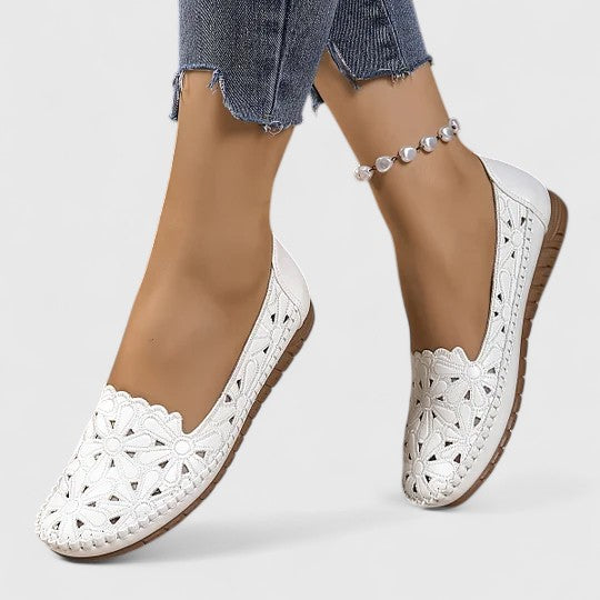 White - Women's slip-on loafers featuring a faux-leather upper with intricate floral cutouts and a flat, textured sole.