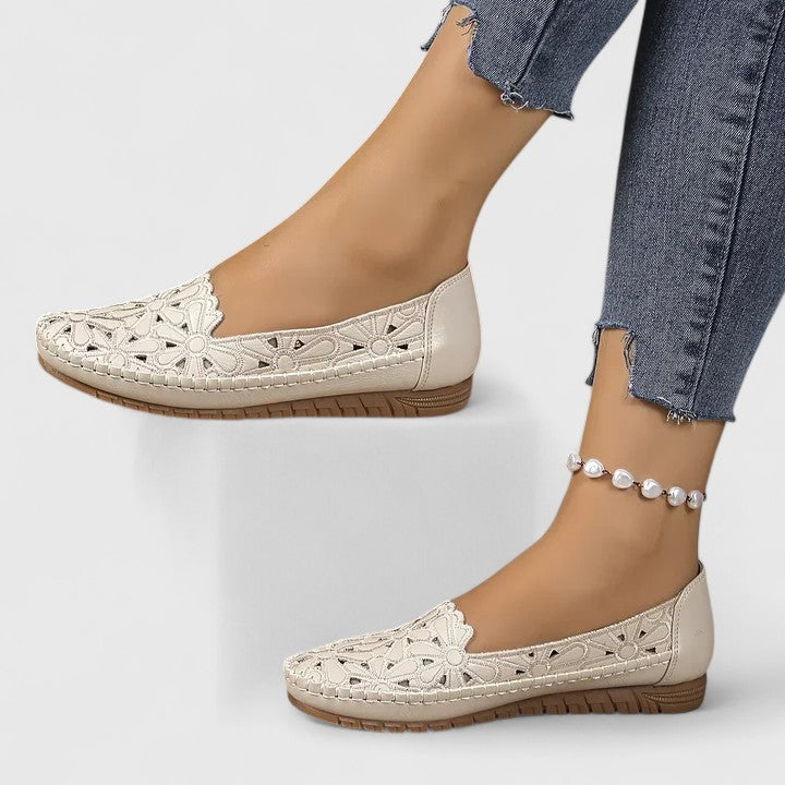 White - Women's slip-on loafers featuring a faux-leather upper with intricate floral cutouts and a flat, textured sole.