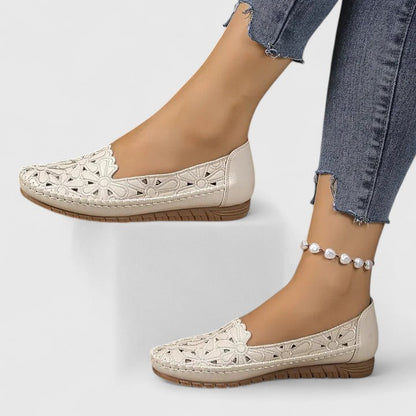 White - Women's slip-on loafers featuring a faux-leather upper with intricate floral cutouts and a flat, textured sole.