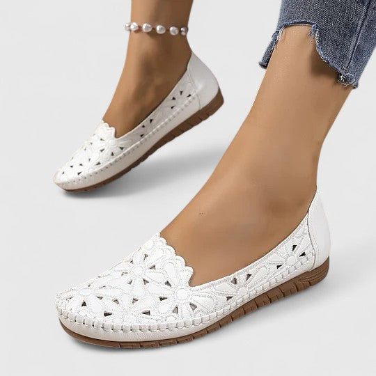 White - Women's slip-on loafers featuring a faux-leather upper with intricate floral cutouts and a flat, textured sole.
