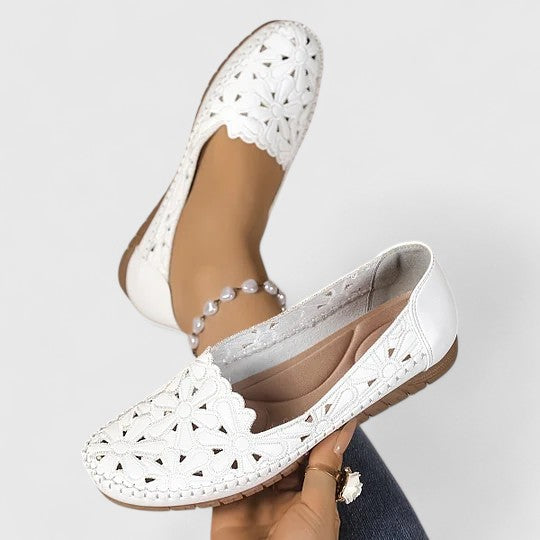 White - Women's slip-on loafers featuring a faux-leather upper with intricate floral cutouts and a flat, textured sole.