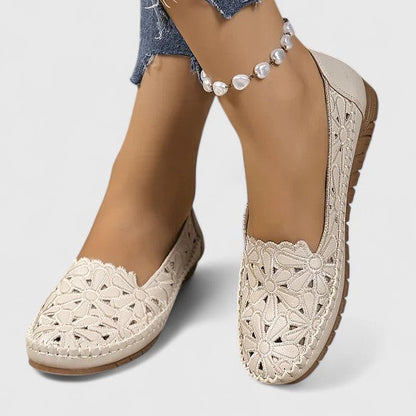 White - Women's slip-on loafers featuring a faux-leather upper with intricate floral cutouts and a flat, textured sole.