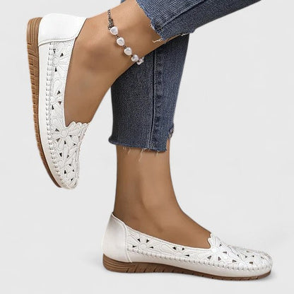 White - Women's slip-on loafers featuring a faux-leather upper with intricate floral cutouts and a flat, textured sole.