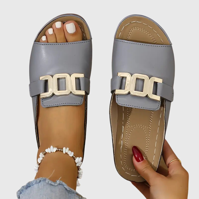 Gray - Women's faux-leather open-toe slide sandals featuring a contoured footbed, slight wedge sole, and prominent metallic buckle hardware across the vamp.