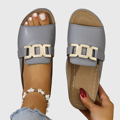 Gray - Women's faux-leather open-toe slide sandals featuring a contoured footbed, slight wedge sole, and prominent metallic buckle hardware across the vamp.