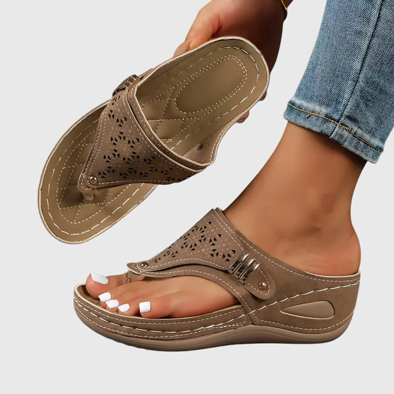 Brown - Faux-leather wedge sandals featuring a slip-on thong design, laser-cut upper detailing, decorative metallic buckle, and prominent contrast stitching along a thick shock-absorbing sole.