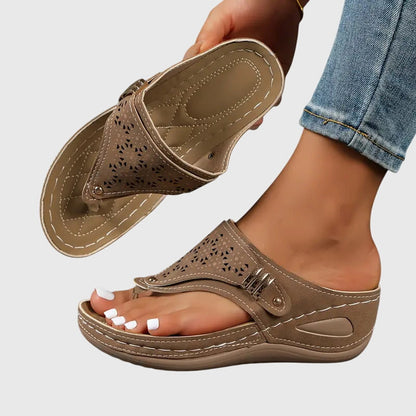 Brown - Faux-leather wedge sandals featuring a slip-on thong design, laser-cut upper detailing, decorative metallic buckle, and prominent contrast stitching along a thick shock-absorbing sole.