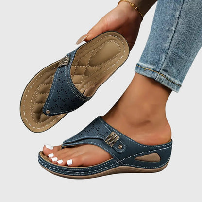 Navy - Faux-leather wedge sandals featuring a slip-on thong design, laser-cut upper detailing, decorative metallic buckle, and prominent contrast stitching along a thick shock-absorbing sole.