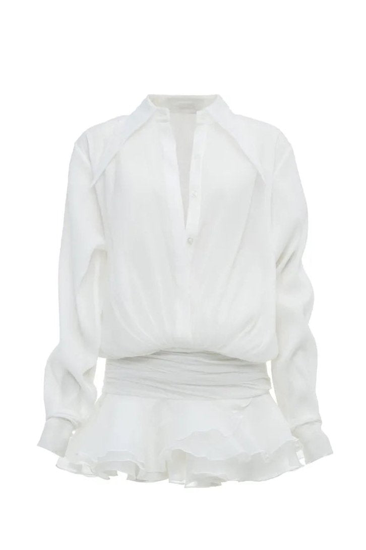 Front view of a woman wearing a sheer white mini shirt dress featuring a pointed collar, blouson top, wide ruched waist, and a short, tiered ruffled skirt.