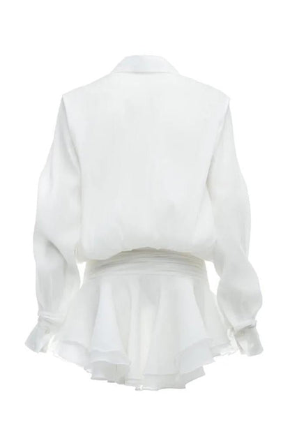 Front view of a woman wearing a sheer white mini shirt dress featuring a pointed collar, blouson top, wide ruched waist, and a short, tiered ruffled skirt.