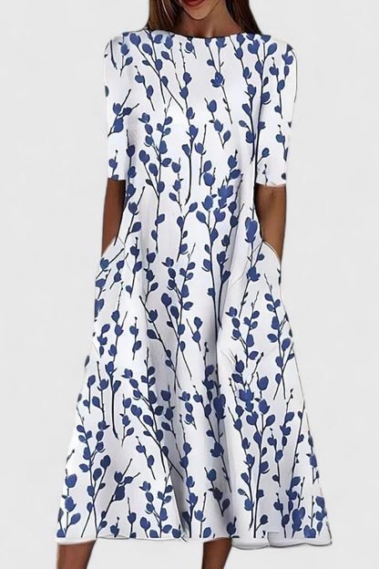 White - A woman wearing a white midi-length A-line dress featuring a blue floral branch print, half sleeves, a boat neckline, and functional side pockets.