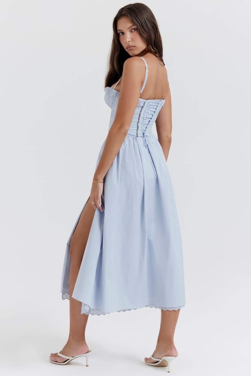 A woman stands against a white background wearing a light blue midi dress with thin spaghetti straps, a fitted eyelet corset bodice with a ruffled neckline, and a flowing A-line skirt with a high thigh slit.