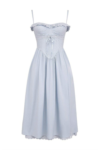 A woman models a light blue midi dress with spaghetti straps, a fitted broderie anglaise corset bodice, a flowing A-line skirt with a high side slit, and a matching broderie anglaise hem.