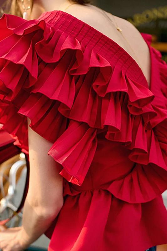 A blonde woman modelling a bright red peplum blouse with dramatic, voluminous ruffles framing a V-neckline, paired with light wash jeans.
