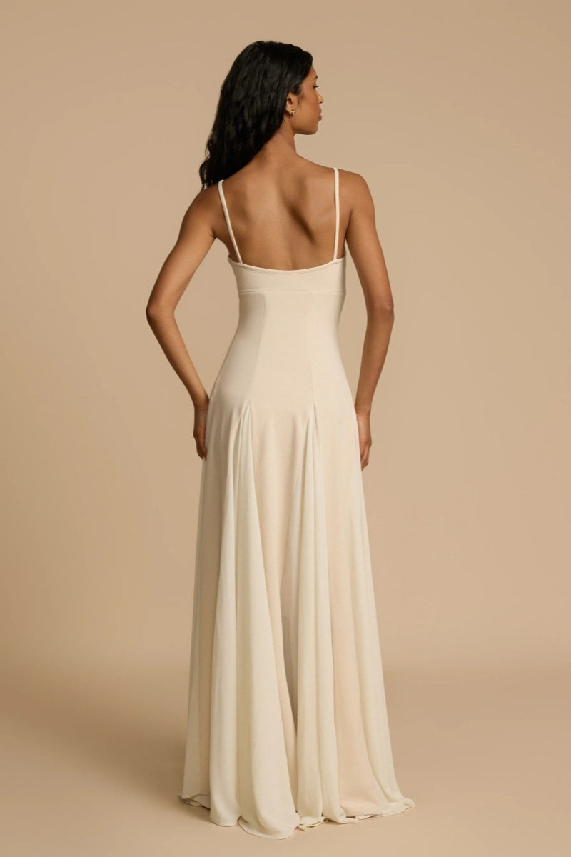 Full-length studio shot of a woman wearing a cream-colored A-line maxi dress with spaghetti straps, a sweetheart bustier bodice, and a voluminous, flowing skirt spread out at the hem.