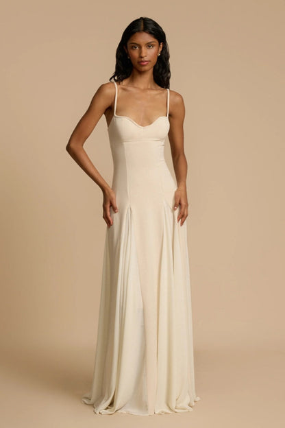 Full-length studio shot of a woman wearing a cream-colored A-line maxi dress with spaghetti straps, a sweetheart bustier bodice, and a voluminous, flowing skirt spread out at the hem.