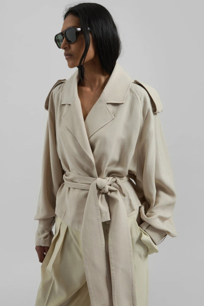 Women's cropped wrap trench jacket featuring a self-tie waist belt, wide lapels, shoulder epaulettes, and adjustable cuff straps in a fluid, relaxed fit.