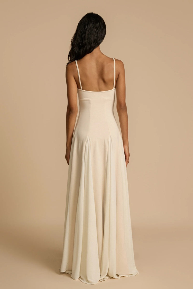 Full-length studio shot of a woman wearing a cream-colored A-line maxi dress with spaghetti straps, a sweetheart bustier bodice, and a voluminous, flowing skirt spread out at the hem.