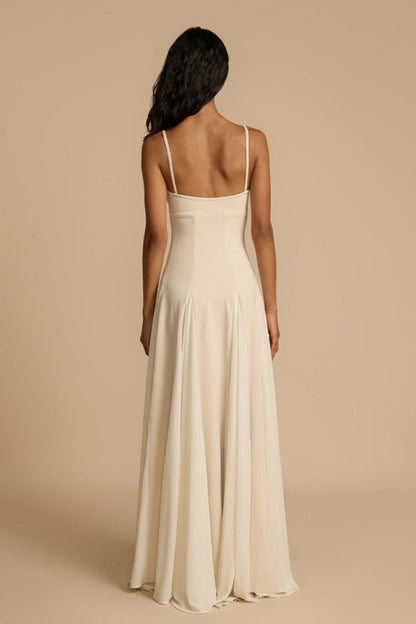 Full-length studio shot of a woman wearing a cream-colored A-line maxi dress with spaghetti straps, a sweetheart bustier bodice, and a voluminous, flowing skirt spread out at the hem.