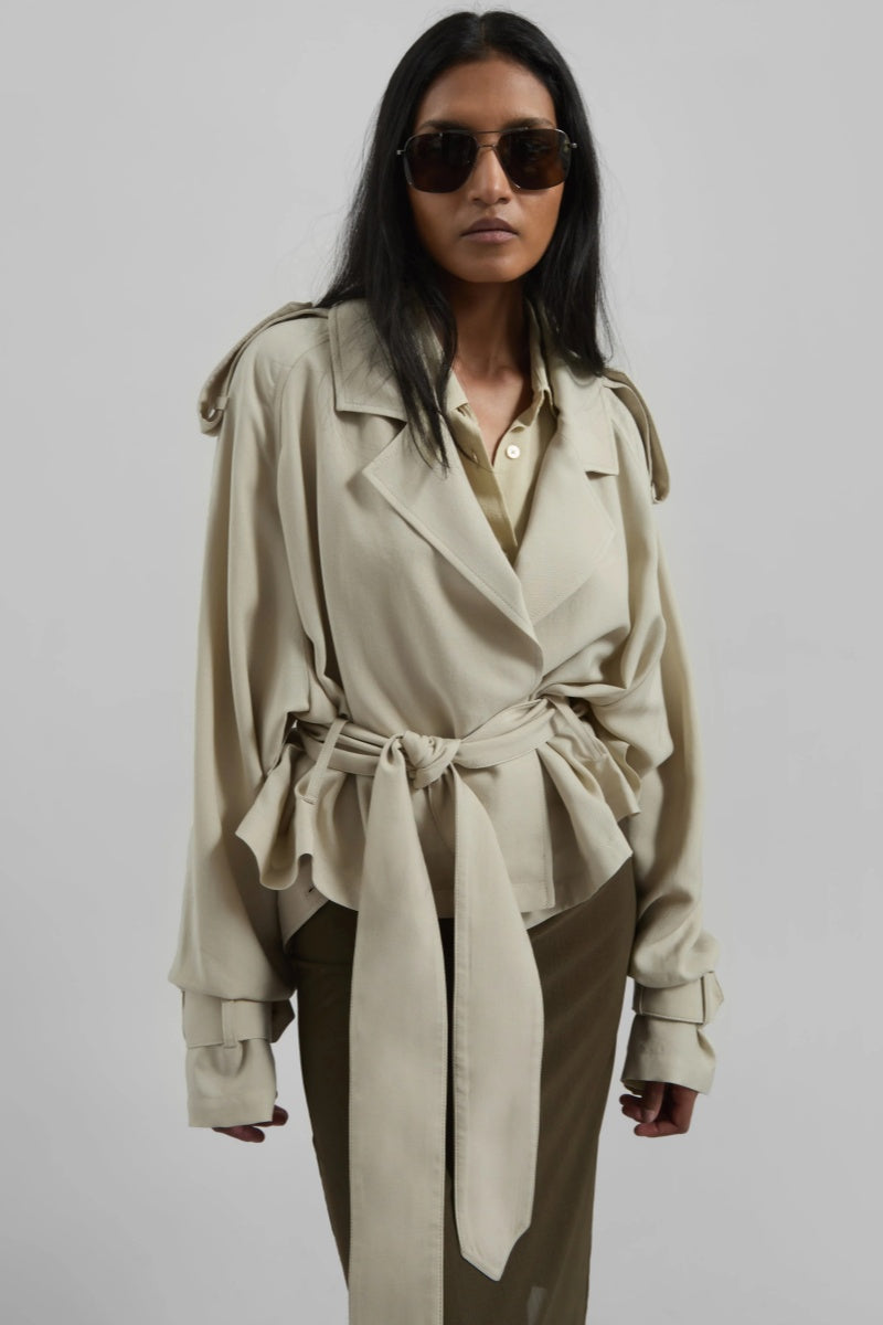 Women's cropped wrap trench jacket featuring a self-tie waist belt, wide lapels, shoulder epaulettes, and adjustable cuff straps in a fluid, relaxed fit.
