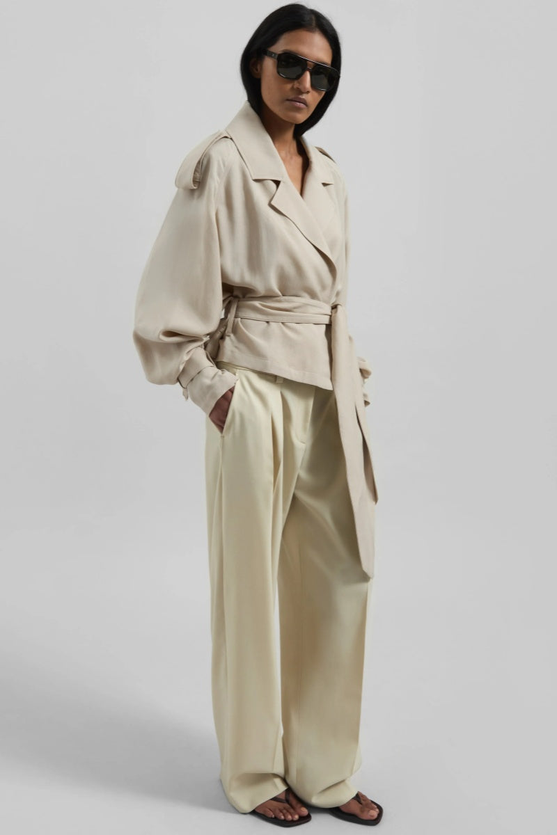 Women's cropped wrap trench jacket featuring a self-tie waist belt, wide lapels, shoulder epaulettes, and adjustable cuff straps in a fluid, relaxed fit.