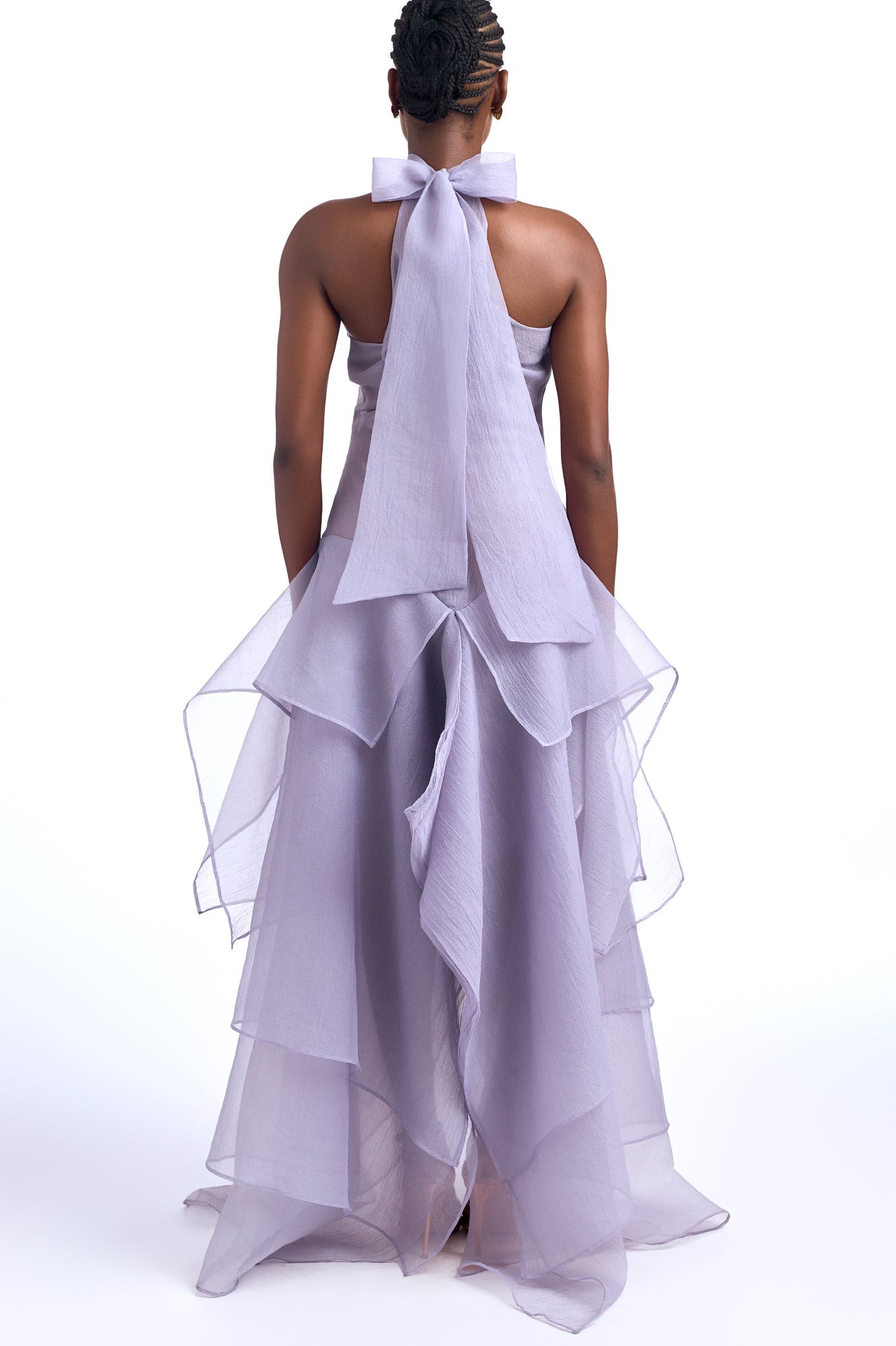 Purple - A woman wearing an elegant, floor-length gown featuring a high halter neckline, an asymmetrical layered bodice, and a voluminous tiered skirt made of sheer, crisp fabric.
