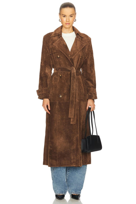 Brown - A woman wearing a longline, double-breasted brown suede trench coat with a self-tie waist belt, notched lapels, and cuff straps, styled over wide-leg blue jeans.