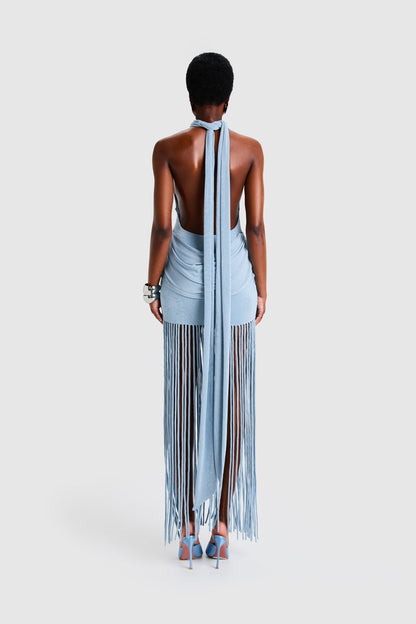 Full-length studio shot of a Black model wearing a sleeveless, high-neck halter dress in a deep red. The dress is form-fitting with ruching at the hips and features a dramatic, floor-length hem made of long, thick corded fringe.