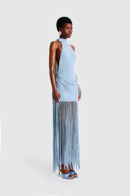 Full-length studio shot of a Black model wearing a sleeveless, high-neck halter dress in a deep red. The dress is form-fitting with ruching at the hips and features a dramatic, floor-length hem made of long, thick corded fringe.
