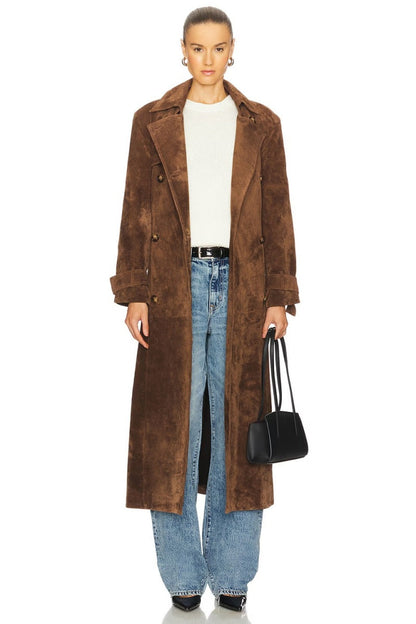 Brown - A woman wearing a longline, double-breasted brown suede trench coat with a self-tie waist belt, notched lapels, and cuff straps, styled over wide-leg blue jeans.
