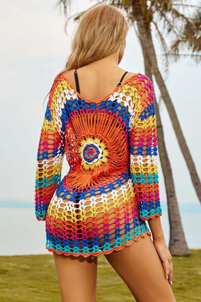 Multicolor - A woman models a long-sleeved, multi-colored crochet tunic cover-up with a central sunburst medallion pattern over a black bikini top, standing on a grassy lawn with palm trees in the background.