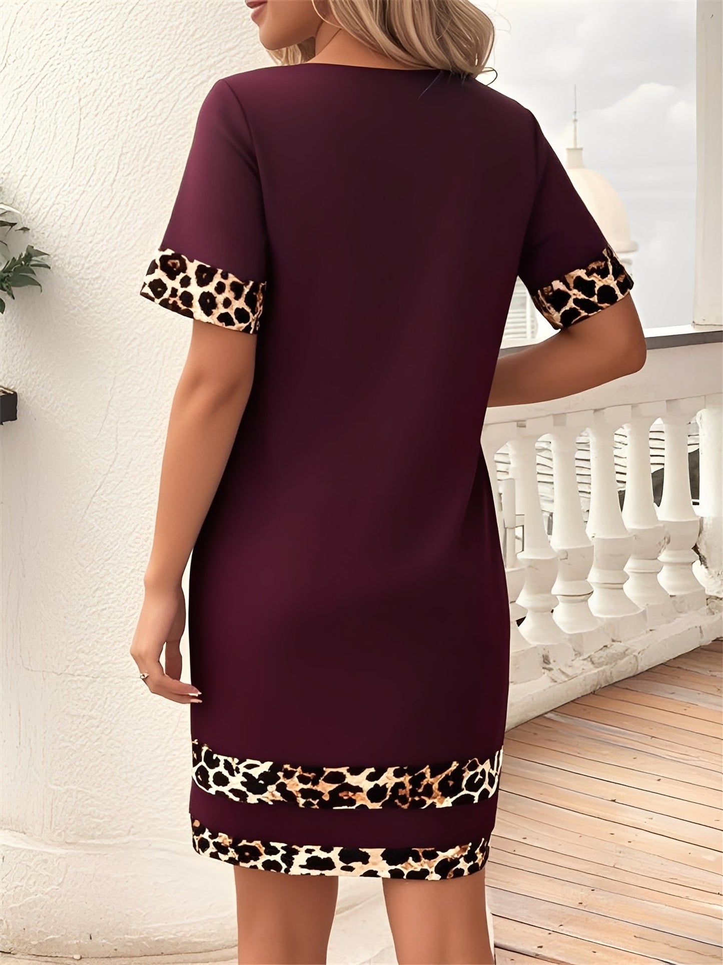 Burgundy - Woman wearing a short-sleeve shift mini dress with leopard print trim on the sleeves and hem, holding a small handbag