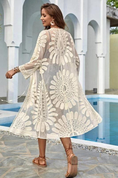 Woman wearing a white semi-sheer lace kimono cover-up with intricate floral patterns over a black bikini.