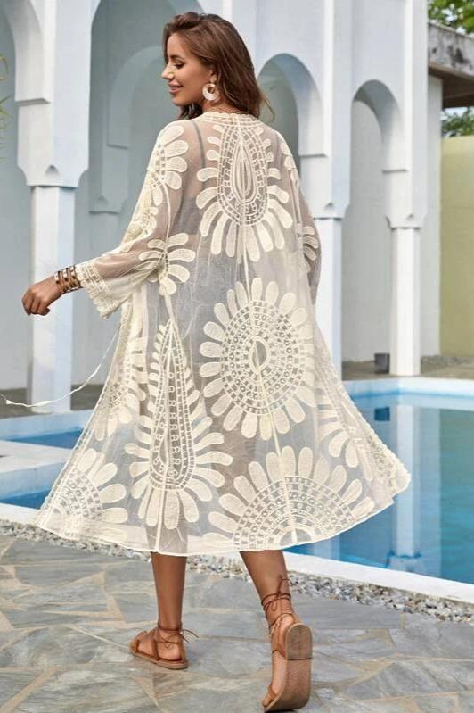 White - A woman models a sheer white, knee-length, open-front cover-up featuring bold floral lace embroidery over a black bikini.