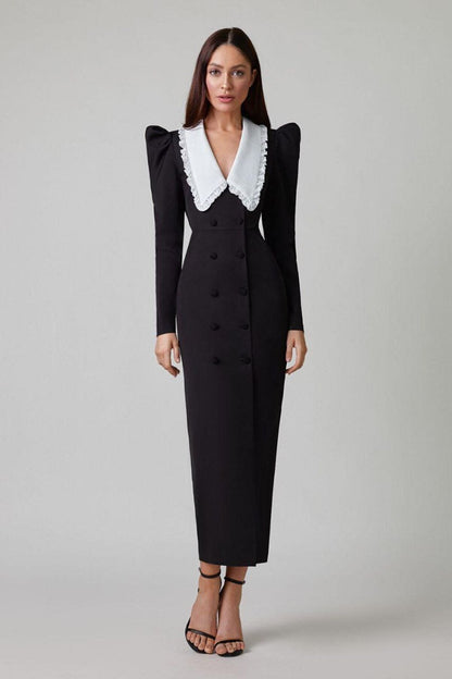 A woman models a long-sleeved, form-fitting black midi dress featuring a double-breasted front, structured puff shoulders, and a large, contrasting white collar with a ruffle edge.
