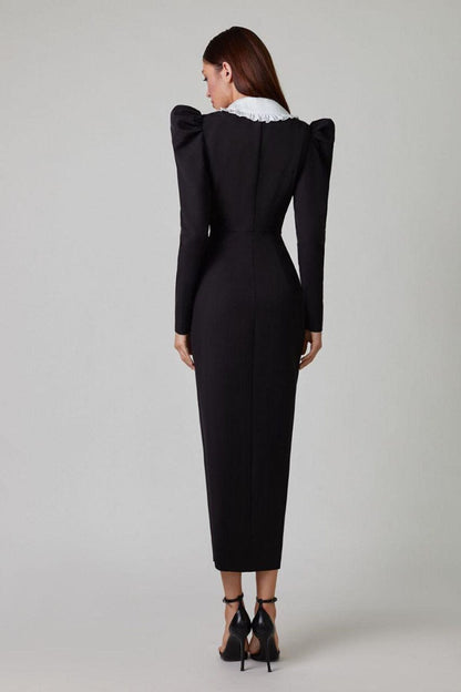 A woman models a long-sleeved, form-fitting black midi dress featuring a double-breasted front, structured puff shoulders, and a large, contrasting white collar with a ruffle edge.