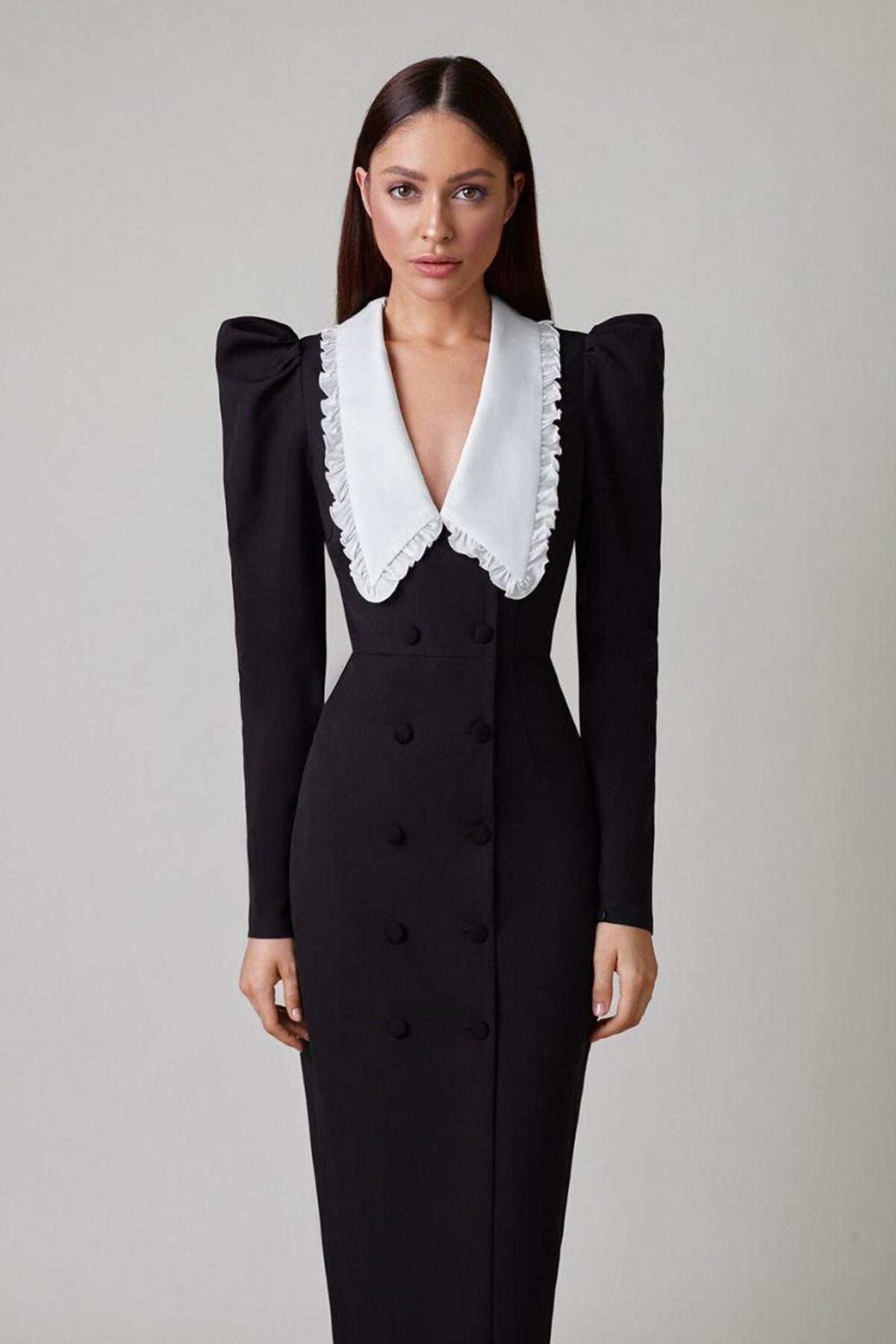 Black - A woman models a long-sleeved, form-fitting black midi dress featuring a double-breasted front, structured puff shoulders, and a large, contrasting white collar with a ruffle edge.
