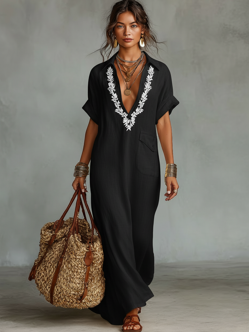 Black - Woman wearing a relaxed-fit, floor-length linen maxi dress featuring a deep V-neckline, collar, short sleeves, front patch pocket, and intricate contrast embroidery around the neck.