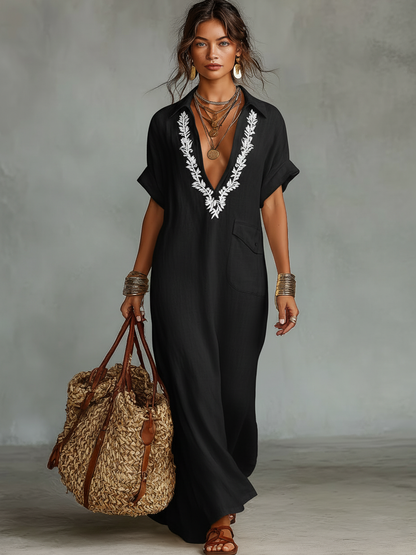 Black - Woman wearing a relaxed-fit, floor-length linen maxi dress featuring a deep V-neckline, collar, short sleeves, front patch pocket, and intricate contrast embroidery around the neck.