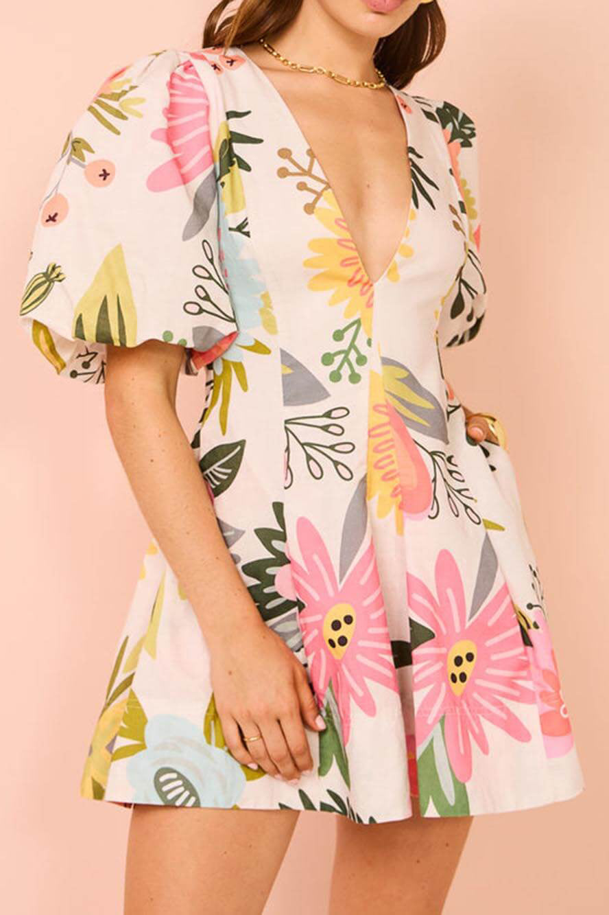 White - A woman wearing a white linen mini dress with a vibrant pink and yellow botanical print, featuring a deep V-neckline and voluminous puff sleeves.