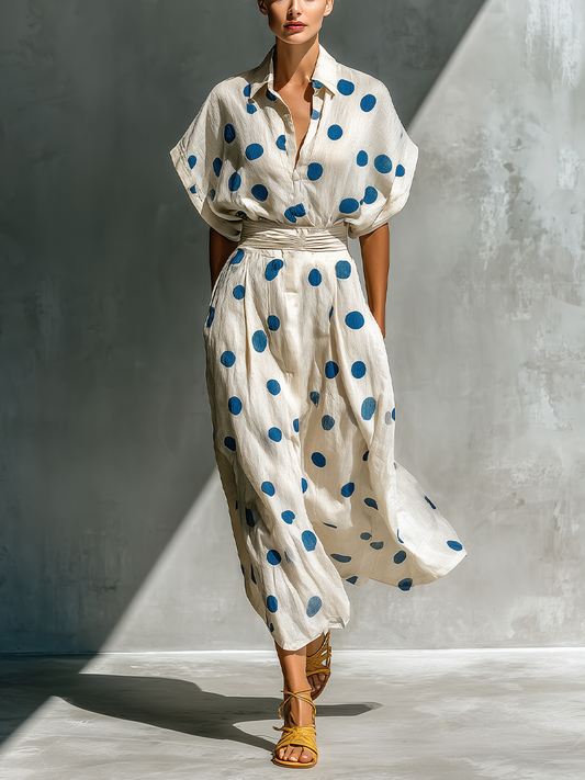 Off-White - Model walking in a flowing dotted midi dress featuring a collared V-neckline, short dolman sleeves, and a wide ruched waistband.