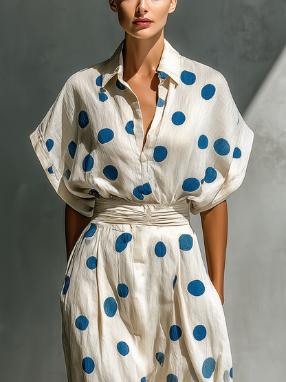 Off-White - Model walking in a flowing dotted midi dress featuring a collared V-neckline, short dolman sleeves, and a wide ruched waistband.