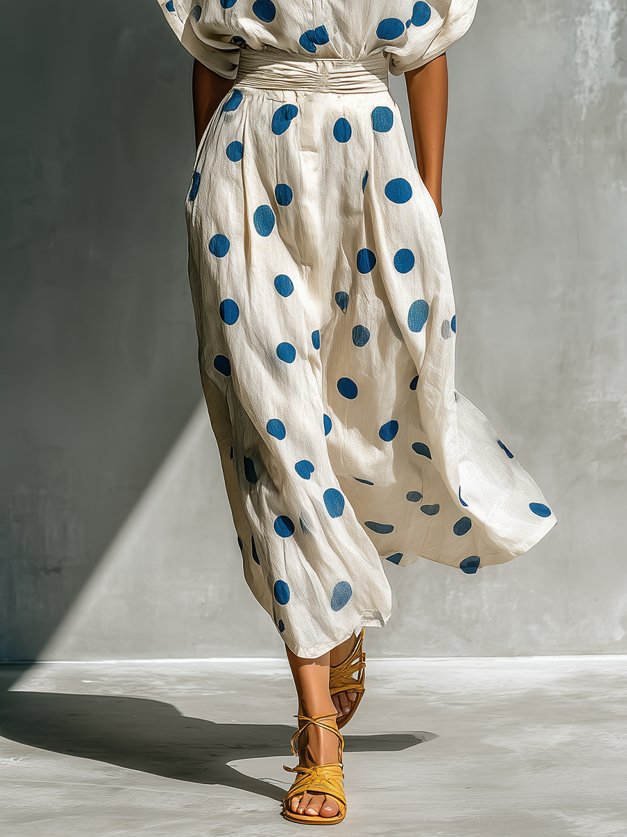 Off-White - Model walking in a flowing dotted midi dress featuring a collared V-neckline, short dolman sleeves, and a wide ruched waistband.