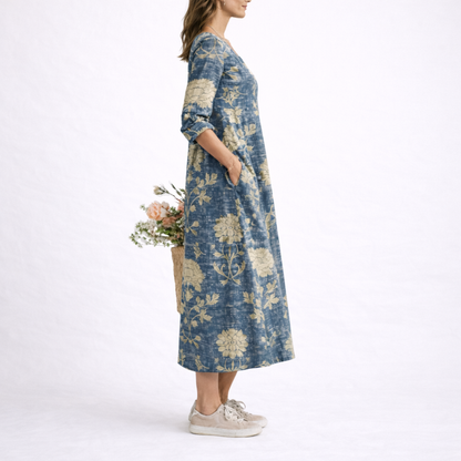 Blue - Model wearing a relaxed fit floral print V-neck midi dress with three-quarter sleeves, holding a woven basket filled with flowers.