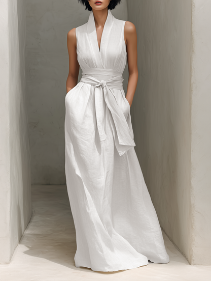 White - Woman wearing a minimalist sleeveless wide-leg jumpsuit with a deep V-neckline and a wide self-tie belt at the waist, posing in an architectural setting.