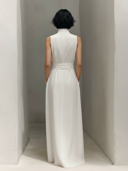 White - Woman wearing a minimalist sleeveless wide-leg jumpsuit with a deep V-neckline and a wide self-tie belt at the waist, posing in an architectural setting.